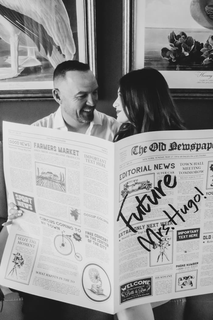 Odette and Morné sharing a smile behind their Future Mr & Mrs Hugo newspaper.